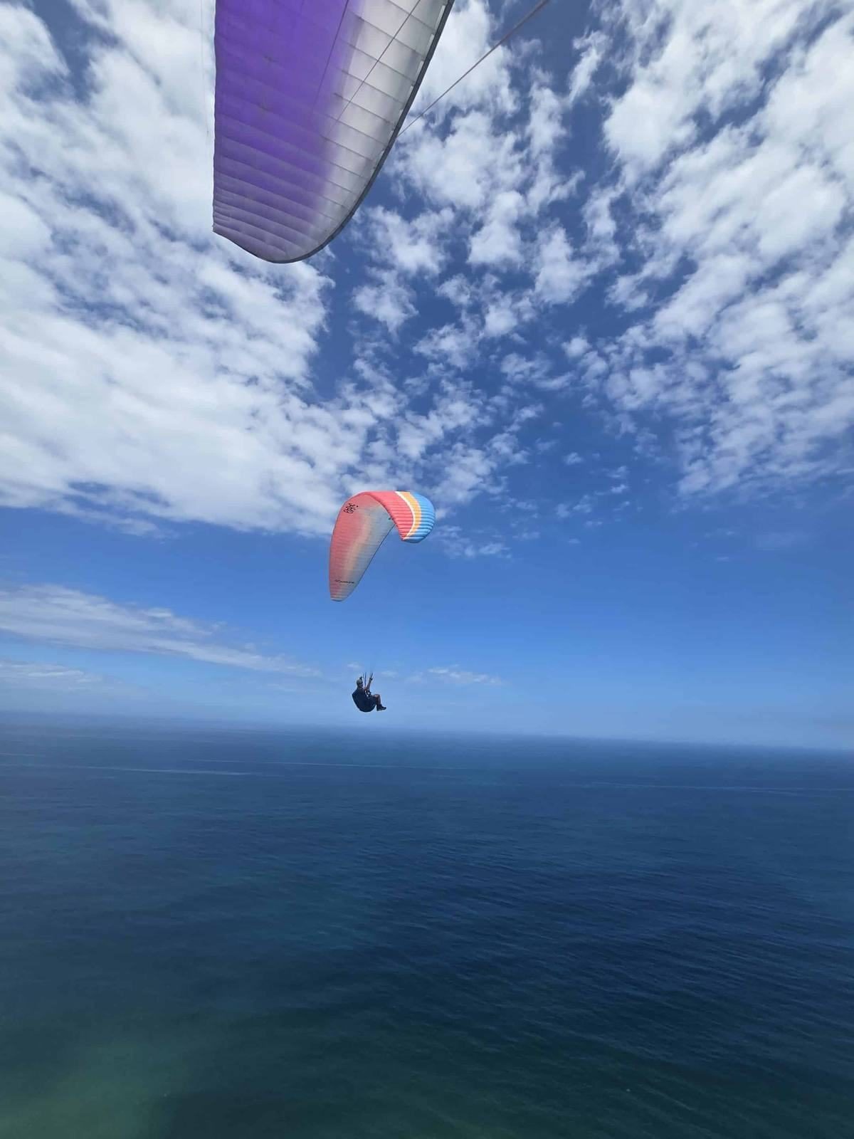 A paraglider with an orange wing flying above the Indian Ocean